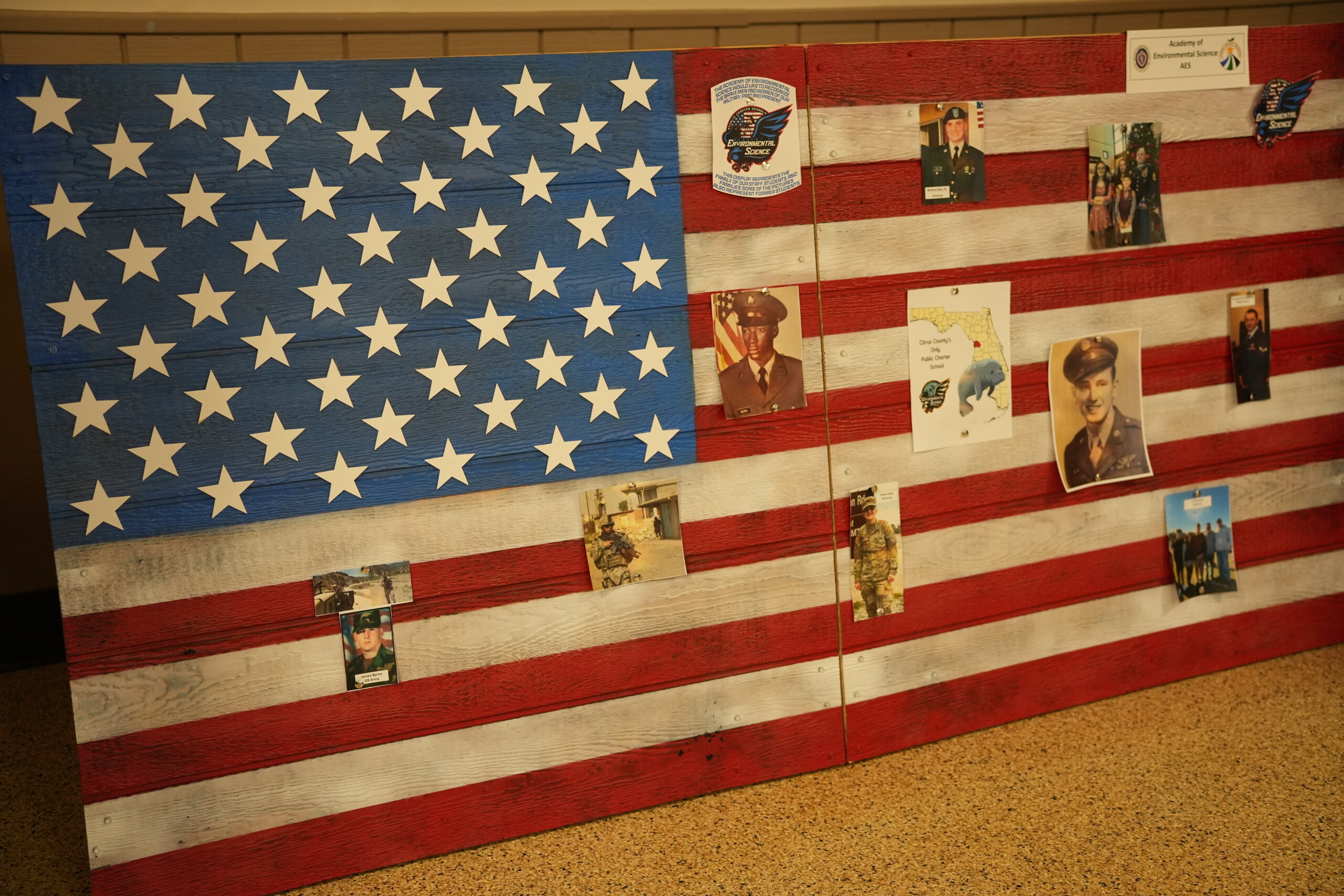A wooden American flag display features painted red, white, and blue boards with attached photographs.